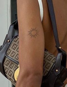 the back of a woman's shoulder with a sun tattoo on her left arm