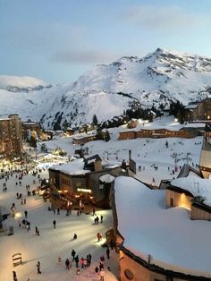 people are walking around in the snow near buildings and mountains with lights on them at night