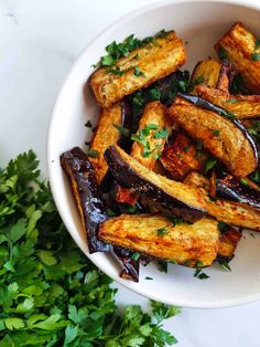 a white bowl filled with cooked eggplant and parsley on top of a table