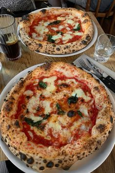 two pizzas sitting on top of white plates on a table next to each other