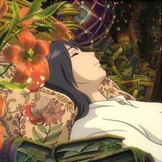 a woman laying on top of a bed in front of flowers and plants with her eyes closed