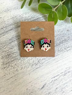 a pair of colorful beaded earrings sitting on top of a wooden table next to a plant