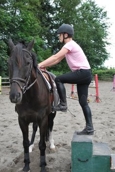 a woman riding on the back of a brown horse next to a green box and trees