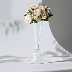 a clear vase with flowers in it on a white tableclothed surface and shadow from the wall