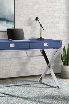 a blue desk with a laptop on it in front of a brick wall and potted plant