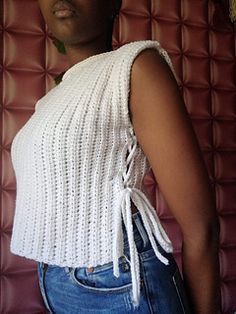 a woman standing in front of a red wall wearing jeans and a white top with laces on it