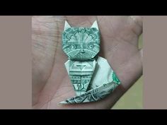 an origami cat sitting on top of a pile of money in someone's hand