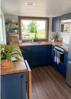 a kitchen with blue cabinets and wood floors, an oven, sink, dishwasher and window