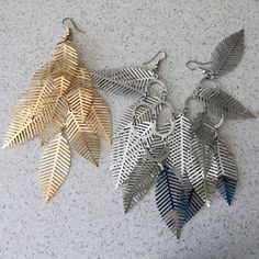 three pairs of leaf shaped metal earrings on a white counter top with blue and gold leaves hanging from them