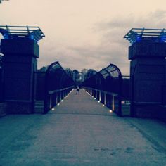 a person walking down a walkway with some lights on it's sides and an open gate at the end