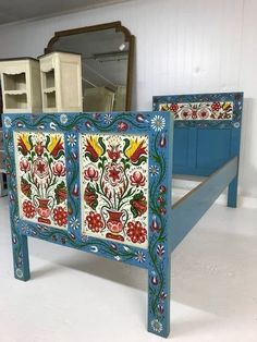 a blue painted bed frame with flowers and leaves on the sides, in front of a mirror