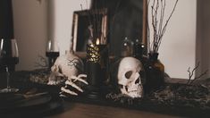 there are two skulls on the table next to some wine glasses and bottles with candles in them