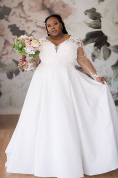 a woman in a white wedding dress holding a flower bouquet and posing for the camera