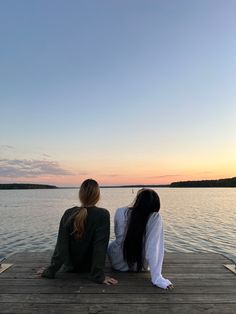 two women sitting on a dock watching the sunset