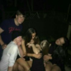 a group of people sitting around each other in a circle at night time, with one person taking a selfie