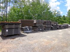 several stacks of wood sitting on top of a gravel road next to trees and bushes