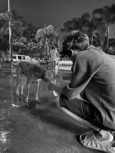 a man kneeling down next to a dog on top of a wet ground with trees in the background