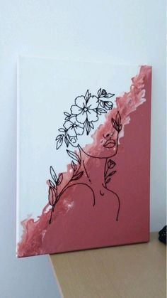 a pink and white painting with flowers on the face is sitting on a table next to a remote control