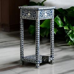 a blue and white table sitting on top of a tiled floor next to a plant