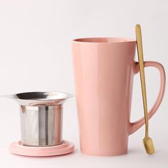 a pink coffee cup next to a metal strainer with a gold spoon in it