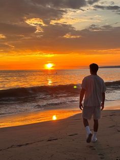 a man standing on top of a sandy beach next to the ocean at sunset,