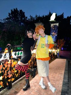 two people dressed in costumes posing for a photo on a brick walkway at night with trees and lights behind them