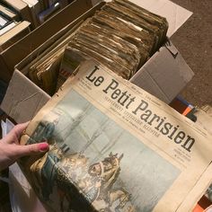 a person is holding up a newspaper in front of stacks of boxes and papers on the ground