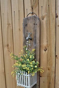 a potted plant is hanging on the side of a wooden fence with a water faucet attached to it