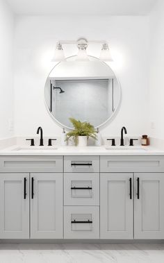 a white bathroom with two sinks and a large round mirror above the double sink vanity