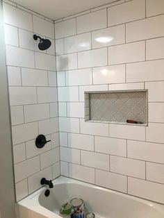 a bathroom with white subway tile and black faucet shower head, toilet paper roll in the bathtub