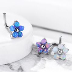 two pairs of opal flower earrings sitting on top of a white surface next to each other