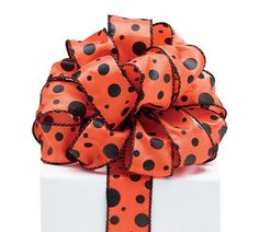 an orange and black polka dot bow on top of a white gift box with ribbon