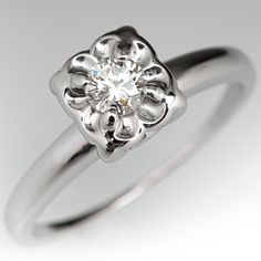 a white gold engagement ring with a flower design on the center, and a round brilliant diamond in the middle