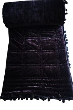 a purple blanket with pom poms on it and a black pillow in the background