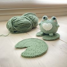 two crocheted frogs sitting next to each other on the floor with balls of yarn