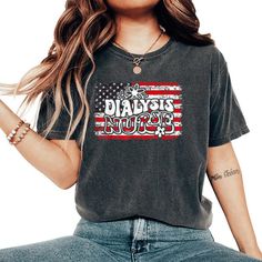 a woman sitting on the ground with her hands in her pockets and wearing an american flag t - shirt