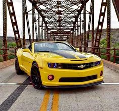 a yellow chevrolet camaro parked on the side of a road under a metal bridge