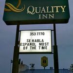 the quality inn sign is lit up in front of it's owner and business name