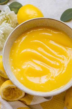 a white bowl filled with yellow liquid next to some lemons