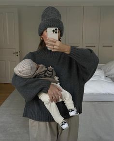 a woman taking a selfie while holding a baby in her arms and wearing a knitted hat