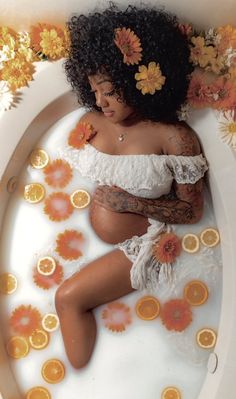 a woman laying in a bathtub with orange flowers around her head and arms on the side