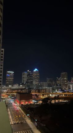 the city skyline is lit up at night with cars driving on the road and buildings in the background