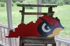 a red and black bird sitting on top of a wooden chair next to a window