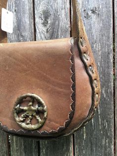 This is a beautifully hand made leather shoulder bag from the 60's or early 1970's hippy era. It has an brass decoration on the front flap. It's beautifully and classically designed. The thick leather is in very good shape, it has scratches from age and wear. There are no rips or tears. The 37" long shoulder strap is thick and strong. This wonderful hippy bag is in very good condition with only minor wear to the leather finish which I consider part of it's charm.The inside is clean. Measures 9.5 Vintage Satchel Shoulder Bag With Metal Hardware, Vintage Crossbody Bag With Metal Hardware, Vintage Leather Bags With Metal Hardware, Vintage Rectangular Saddle Bag With Brass Hardware, Vintage Brown Saddle Bag, Vintage Brown Saddle Bag With Brass Hardware, Vintage Brown Satchel With Brass Hardware, Vintage Everyday Saddle Bag, Vintage Saddle Bag For Everyday Use