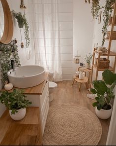 a white bathroom with wooden floors and plants on the wall next to the tub, toilet and sink