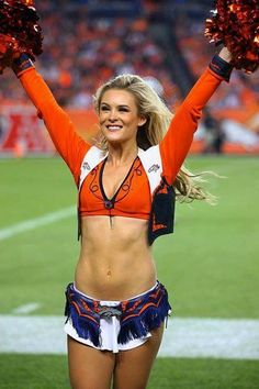 a cheerleader in an orange and white uniform holding her hands up to the sidelines