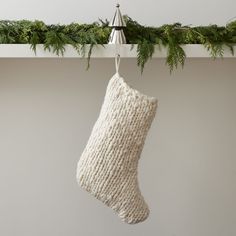 a knitted christmas stocking hanging from a mantel with pine needles on it