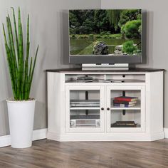 a white entertainment center with glass doors and shelves in front of a large screen tv