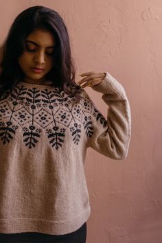 a woman is standing against a wall with her hands on her head and wearing a sweater