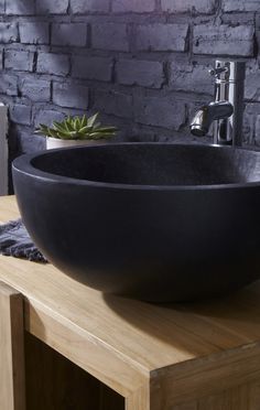 a black bowl sink sitting on top of a wooden counter next to a brick wall